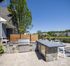 Chic outdoor patio with modern stone grill and dining area, perfect for entertaining against a lush, scenic background.
