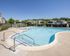 Inviting outdoor pool area with lounge chairs and umbrellas, surrounded by scenic residential homes and lush greenery.