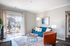 Bright and inviting living room with a stylish blue sofa, cozy armchair, and floor-to-ceiling windows leading to a charming outdoor patio.
