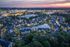 Charming aerial view of a serene residential community at dusk, featuring beautifully lit homes, winding streets, and tranquil water features, with a vibrant city skyline in the distance.