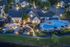 Enchanting aerial view of a luxurious residential complex featuring a beautifully landscaped courtyard with ambient lighting, a pristine swimming pool, and elegant outdoor seating areas.