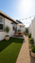 Charming outdoor patio featuring lush artificial grass, elegant potted plants, and a cozy dining area under string lights.