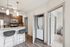 Contemporary kitchen with sleek granite countertop, stylish bar stools, and stacked washer-dryer in a cozy modern apartment.