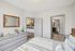 Bright and modern bedroom with sleek gray furnishings, featuring a view into a contemporary bathroom and stylish kitchen bar area.