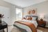 Bright and modern bedroom featuring elegant artwork, cozy bedding, and abundant natural light through large windows, perfect for relaxation.