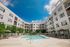 Elegant apartment complex showcasing a refreshing pool surrounded by lush greenery under a bright blue sky.