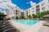 Modern apartment complex with gleaming outdoor pool, surrounded by sun loungers and lush greenery under a clear blue sky.