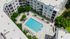 Aerial view of a contemporary apartment complex featuring a sparkling swimming pool, surrounded by lounge chairs and lush greenery, offering a serene urban escape.