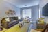 Elegant living room with modern gray sofa, chic wall art, large window with blinds, and stylish coffee table on a yellow rug.
