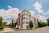 Modern apartment complex with contemporary design, surrounded by lush greenery and a clear blue sky.