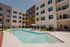 Modern apartment complex showcasing a sparkling outdoor pool surrounded by stylish lounge chairs and vibrant greenery.