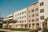 Contemporary apartment building with sleek design, large windows, and vibrant landscaping under a clear blue sky.