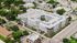 Aerial view of a modern, U-shaped apartment complex surrounded by lush greenery and urban landscape.