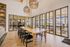 Bright and airy communal space with a large wooden table, chic black chairs, and woven pendant lights, featuring expansive glass doors opening to a sunny outdoor patio.
