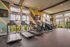 Modern fitness center with treadmills, ellipticals, and stationary bikes, featuring vibrant geometric wall design and large windows with natural light.