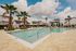 Luxurious outdoor pool area with palm trees and elegant lounge chairs, surrounded by charming modern homes under a vibrant blue sky.