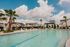 Luxury residential pool area with palm trees and lounge chairs under a vibrant blue sky, offering a resort-style living experience.