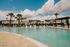 Luxurious swimming pool surrounded by palm trees and elegant white houses under a vibrant blue sky, offering a relaxing oasis in a modern residential community.