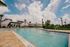 Luxurious outdoor swimming pool with sparkling water, surrounded by palm trees and elegant lounge chairs under a radiant blue sky.