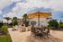 Charming outdoor patio with modern furniture, large umbrellas, and a BBQ station, perfect for entertaining under sunny skies.