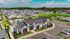Vibrant aerial view of a modern residential community featuring stylish homes, well-manicured lawns, and a central pool area under a bright blue sky.