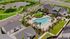 Aerial view of a luxurious residential complex featuring a large swimming pool, modern clubhouse, and lush green landscaping, surrounded by serene water features.