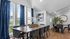 Elegant dining area with a large wooden table, chic black chairs, and vibrant blue curtains offering scenic views. Artistic decor and greenery enhance the sophisticated ambiance.