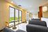 Bright and modern lounge area with large windows, plush gray seating, and chic wooden tables offering soothing views of greenery.