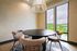 Chic dining area with modern round table and plush chairs, complemented by large windows offering a serene view of lush greenery.
