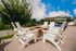 Charming outdoor patio with elegant white chairs surrounding a cozy stone fire pit, perfect for relaxation under a bright blue sky.