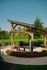 Charming outdoor space featuring a wooden pergola, vibrant red flowers, and lush greenery next to a serene pond.