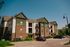 Charming modern apartment building with elegant brick and green facade, ample parking and inviting balconies, surrounded by lush greenery.