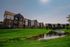 Charming multi-story apartment complex nestled by a serene pond, surrounded by lush green lawns under a clear sky.