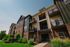 Charming brick and siding apartment complex with private balconies, surrounded by lush greenery and a clear blue sky.