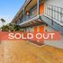 Charming apartment complex with vibrant orange doors and inviting tiled walkway, now sold out.