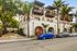 Charming Mediterranean-style apartment building with arched doorways and balconies, surrounded by lush palm trees on a quiet street.