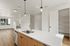 Modern open-concept kitchen with sleek countertops, stylish pendant lighting, and a spacious pantry, leading into a bright living area with natural light.