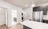 Modern apartment kitchen with sleek dark cabinetry, stainless steel appliances, and an elegant pendant light. Bright bathroom and laundry area are visible, showcasing functional design.