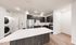Modern kitchen with sleek dark cabinetry, stainless steel appliances, and a spacious quartz countertop island, featuring an in-unit laundry area.