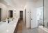 Luxurious modern bathroom with dual sinks, sleek countertop, and elegant lighting, leading to a cozy bedroom with stylish furnishings.
