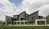 Contemporary apartment complex with modern architecture featuring angular roofs and large windows, set against a lush green landscape and clear skies.