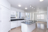 Modern open-concept kitchen and living area with sleek white cabinetry and natural light pouring through large windows.