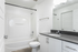 Modern bathroom with sleek white design, featuring a spacious bathtub, large vanity, and elegant fixtures.