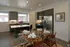 Modern kitchen and dining area featuring sleek stainless steel appliances, elegant glass dining table set for six, and a centerpiece of vibrant purple flowers.
