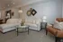 Modern living room featuring a luxurious L-shaped white sofa adorned with patterned cushions, stylish wall decor, and a cozy leather armchair. Warm ambient lighting enhances the inviting atmosphere.
