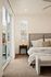 Elegant bedroom with plush carpeting, cozy bed, and a bedside table with stylish lamp, streaming natural light from large sliding glass door.
