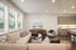 Inviting modern living area with a large beige sectional, patterned cushions, and sleek kitchen featuring ample cabinetry and natural light.