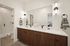 Elegant modern bathroom featuring dual sinks, chic wooden cabinetry, and ambient wall lighting, adjacent to a sleek glass-enclosed shower.