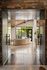 Inviting entrance to a modern living space with large windows, high ceilings, and elegant seating, offering a view of lush greenery.