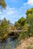 Charming bridge over a picturesque stream surrounded by vibrant autumn foliage and scenic mountain backdrop, under a clear blue sky.